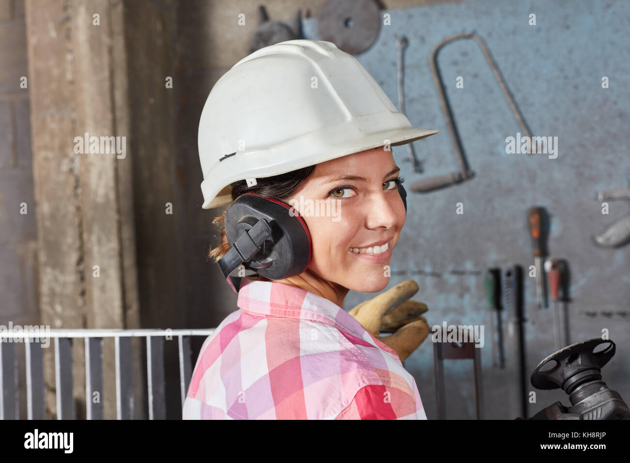Woman as worker apprentice with ear protection and hardhat as labor safety concept Stock Photo