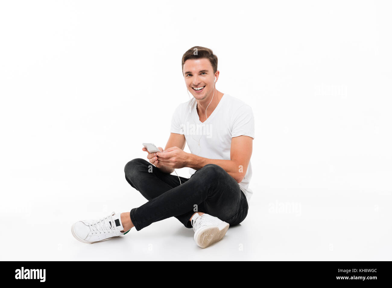 Парень сидит и улыбается. Мужчина сидит на белом фоне. man sitting in a t shirt.