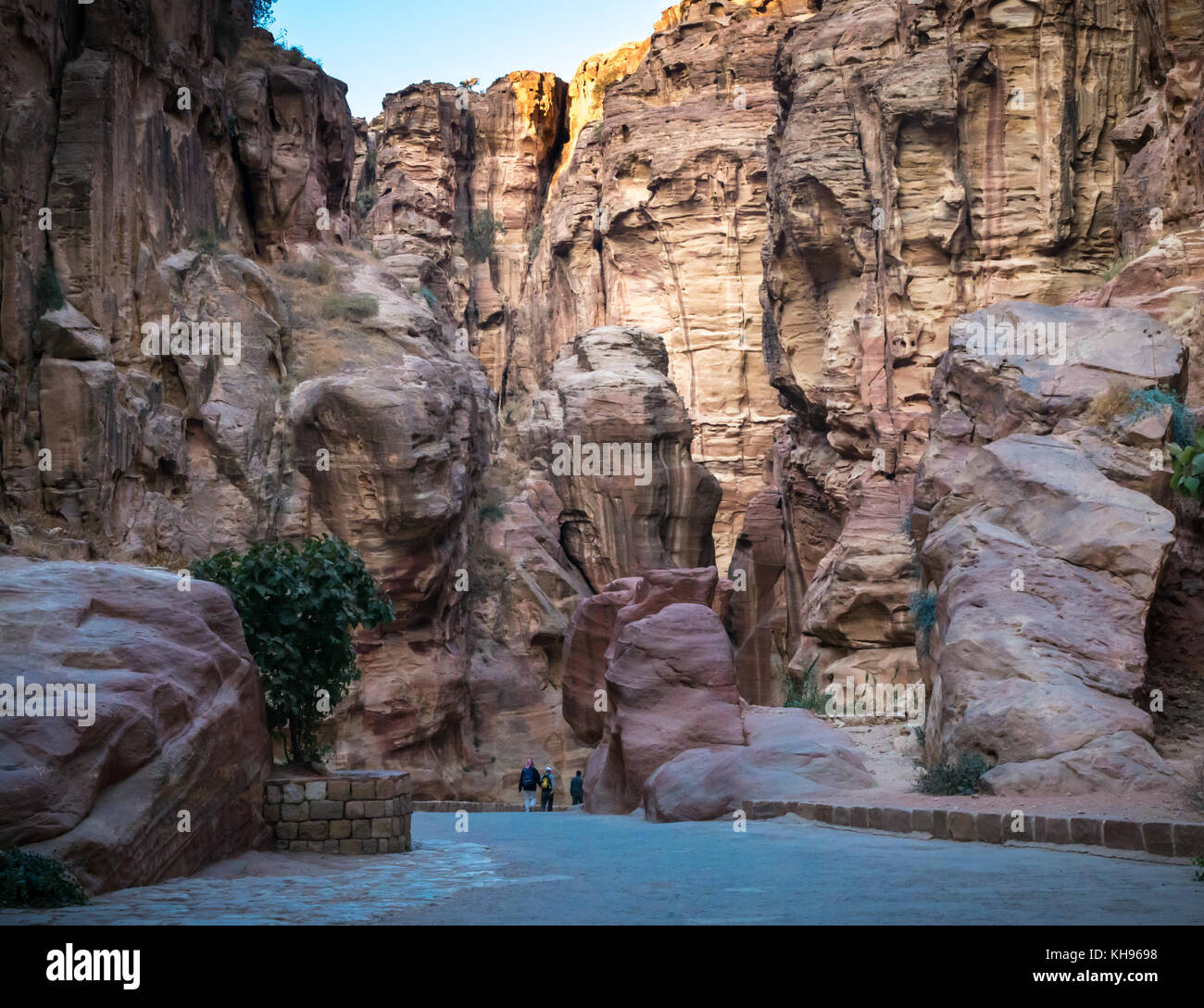 Tourist visitors walking through empty Siq pink sandstone gorge in early morning light, Petra, Jordan, Middle East Stock Photo