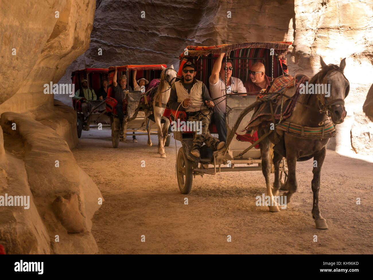 Colourful horse carriages taking tourists through the midday shade of the Siq gorge, Petra, Jordan, Middle East Stock Photo
