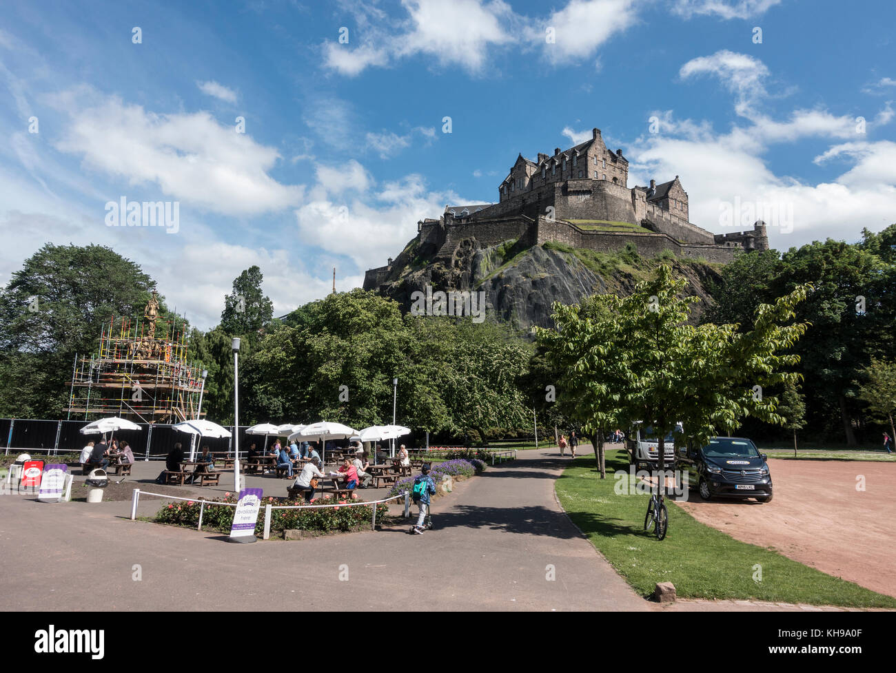 People Enjoy The Summertime Weather At An Outdoor Cafe In West Princes Street Gardens Shadowed By Castle Rock With Edinburgh Castle And The Ross Fount Stock Photo