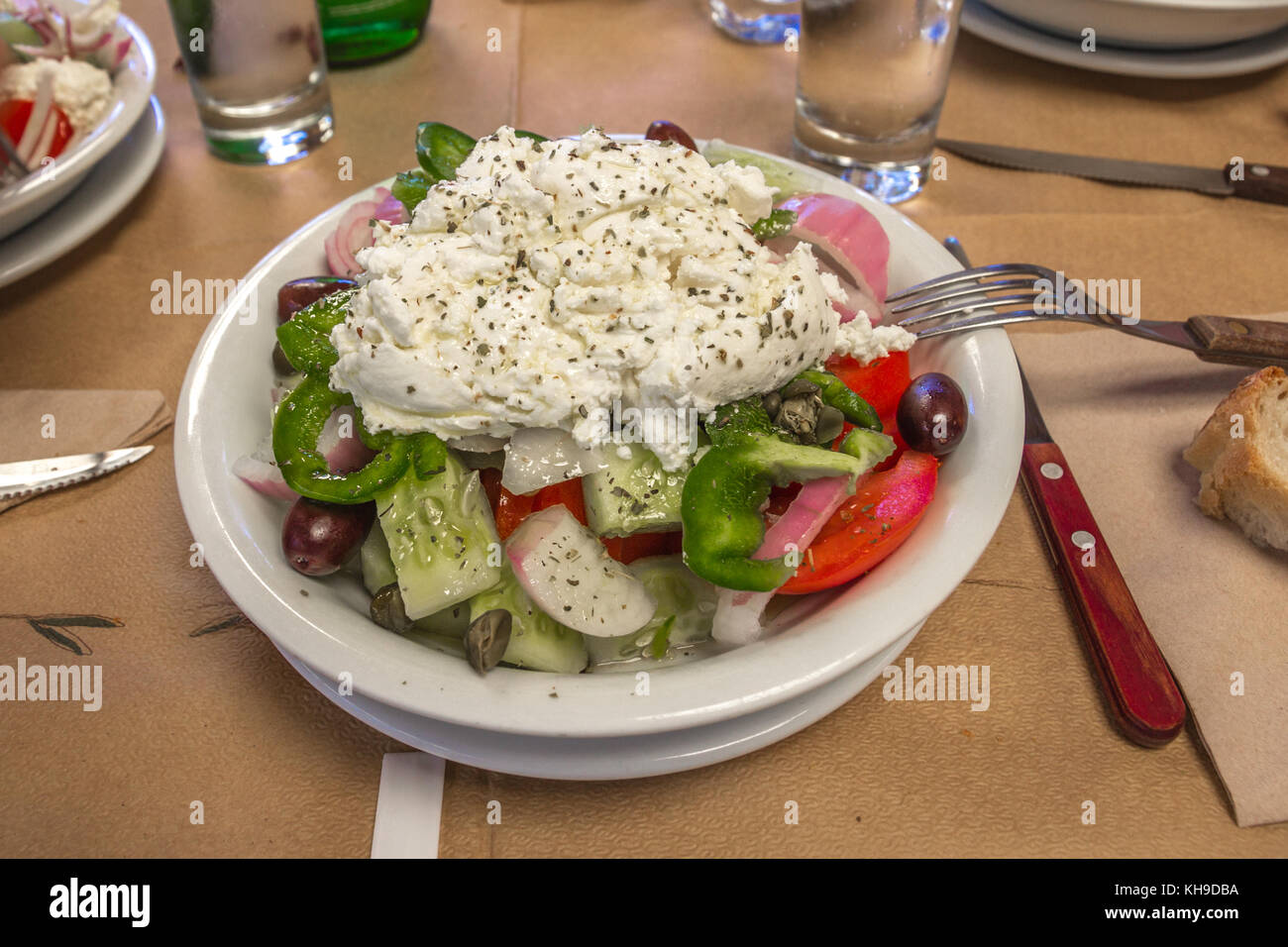 Ready to eat - Greek Salad with fresh tomatoes, cucumbers, red onions, green peppers, olives and a huge dollop of creamy Naxos cheese in a white bowl Stock Photo