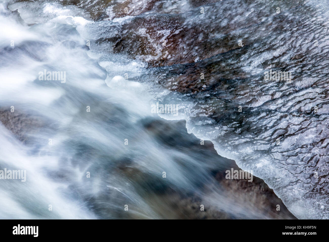 The detailed look at water runs under ice in a river. The snow is ...