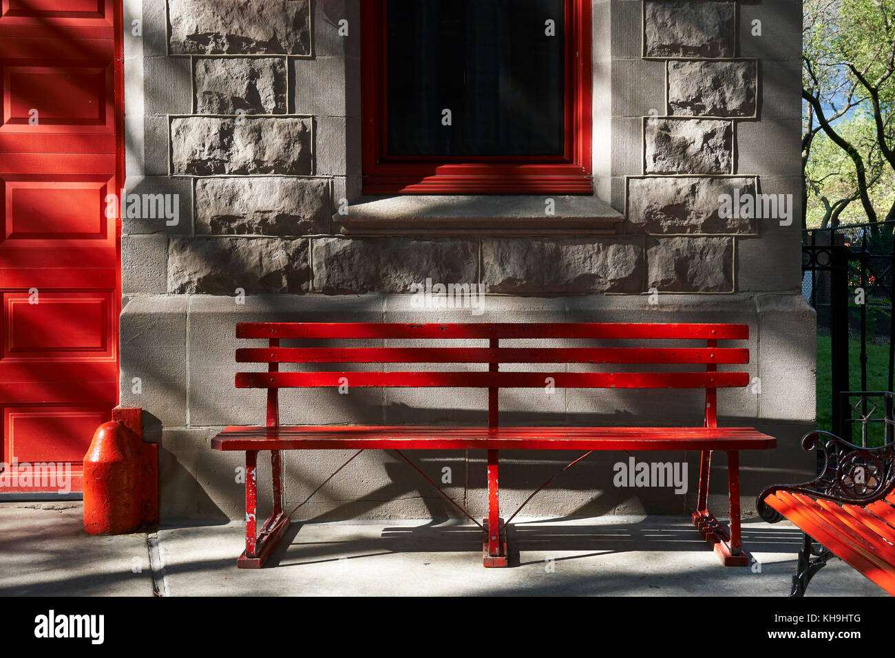 Evening light on red painted bench, under red window frame beside red door against gray stone wall Stock Photo
