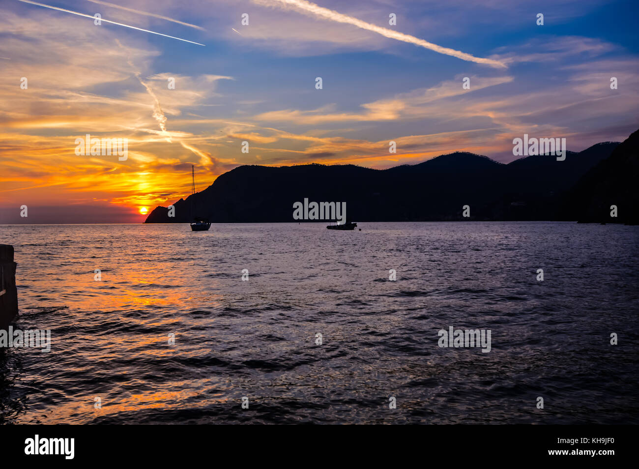 Boats in the beautiful bay of Vernazza in the Ligurian region of Cinque Terra on the northern coast of Italy as the sun sets behind a mountain Stock Photo