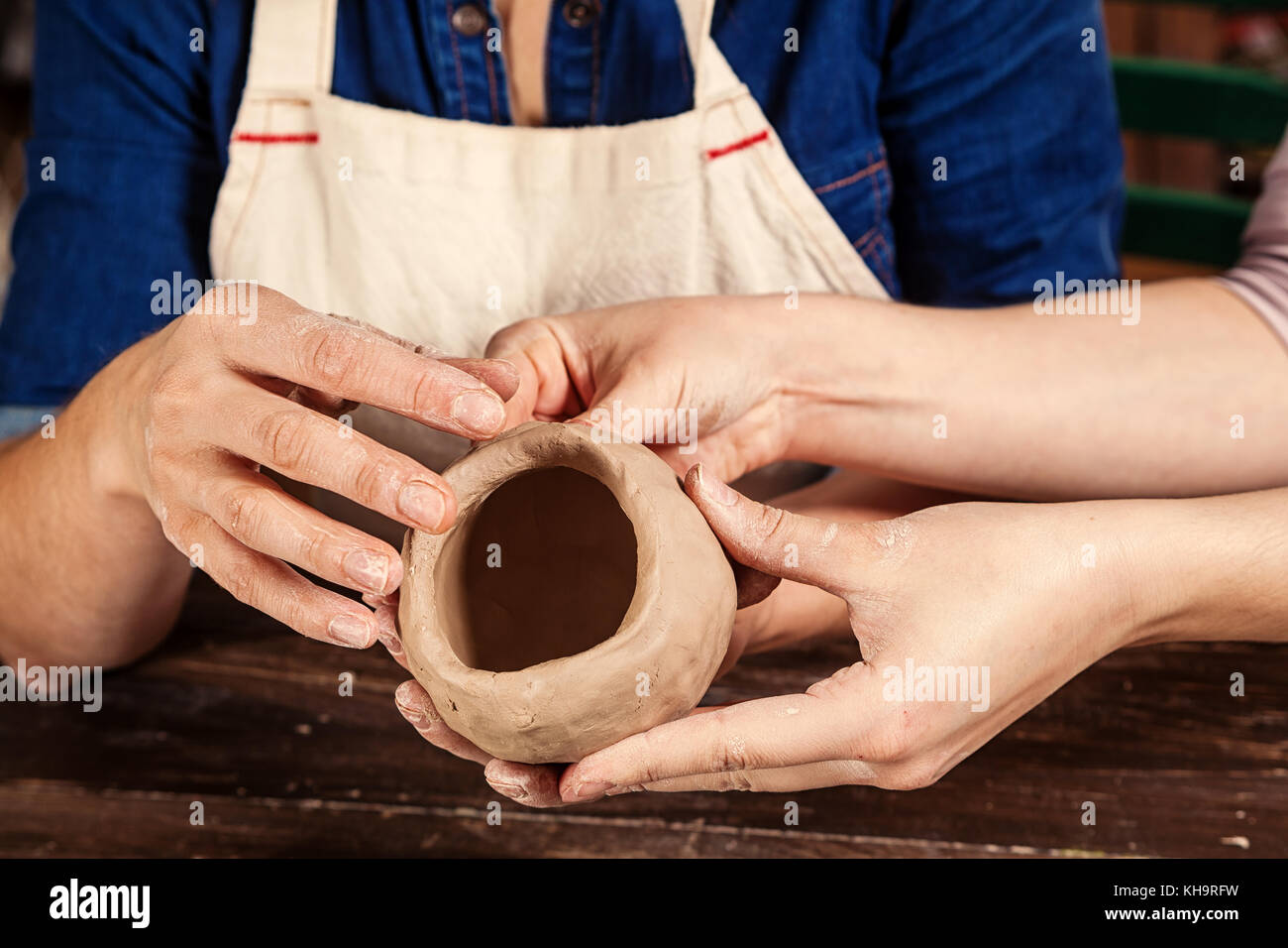 A close-up of a woman potter rolls a brown clay rolling pin on a