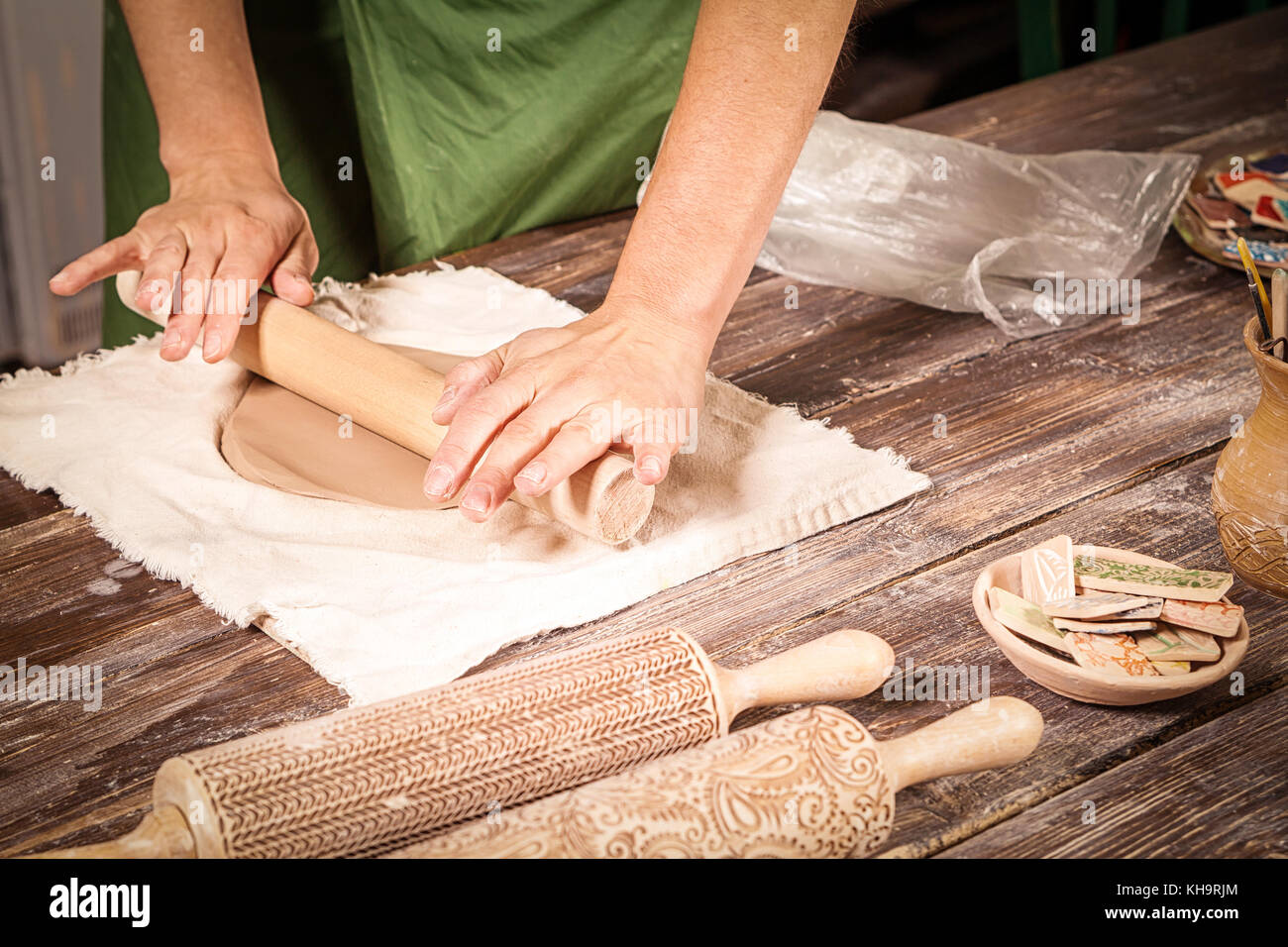 A close-up of a woman potter rolls a brown clay rolling pin on a special  fabric on a wooden table to make a plate and New Year's toys, on the table  li