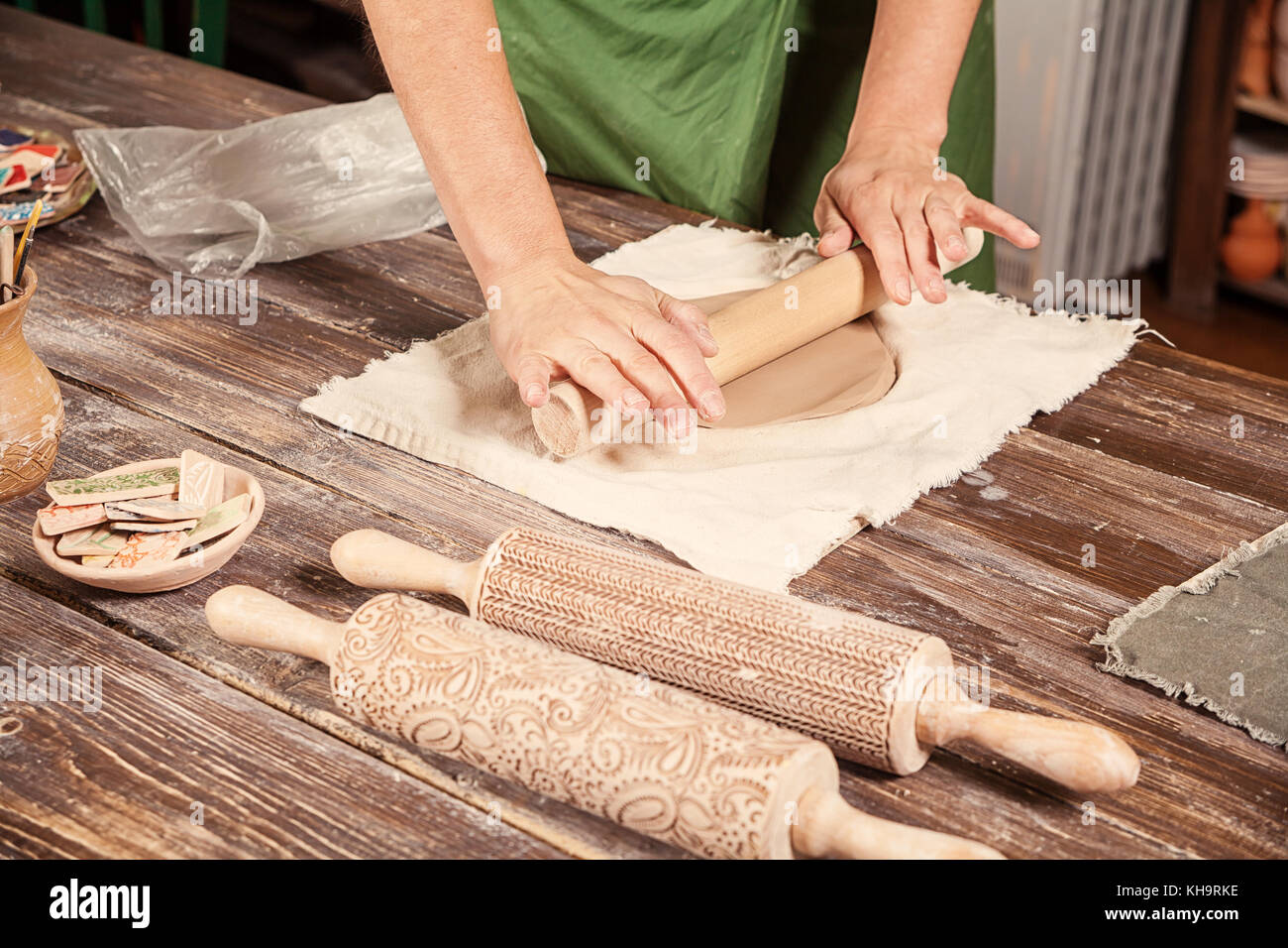A close-up of a woman potter rolls a brown clay rolling pin on a special  fabric on a wooden table to make a plate and New Year's toys, on the table  li