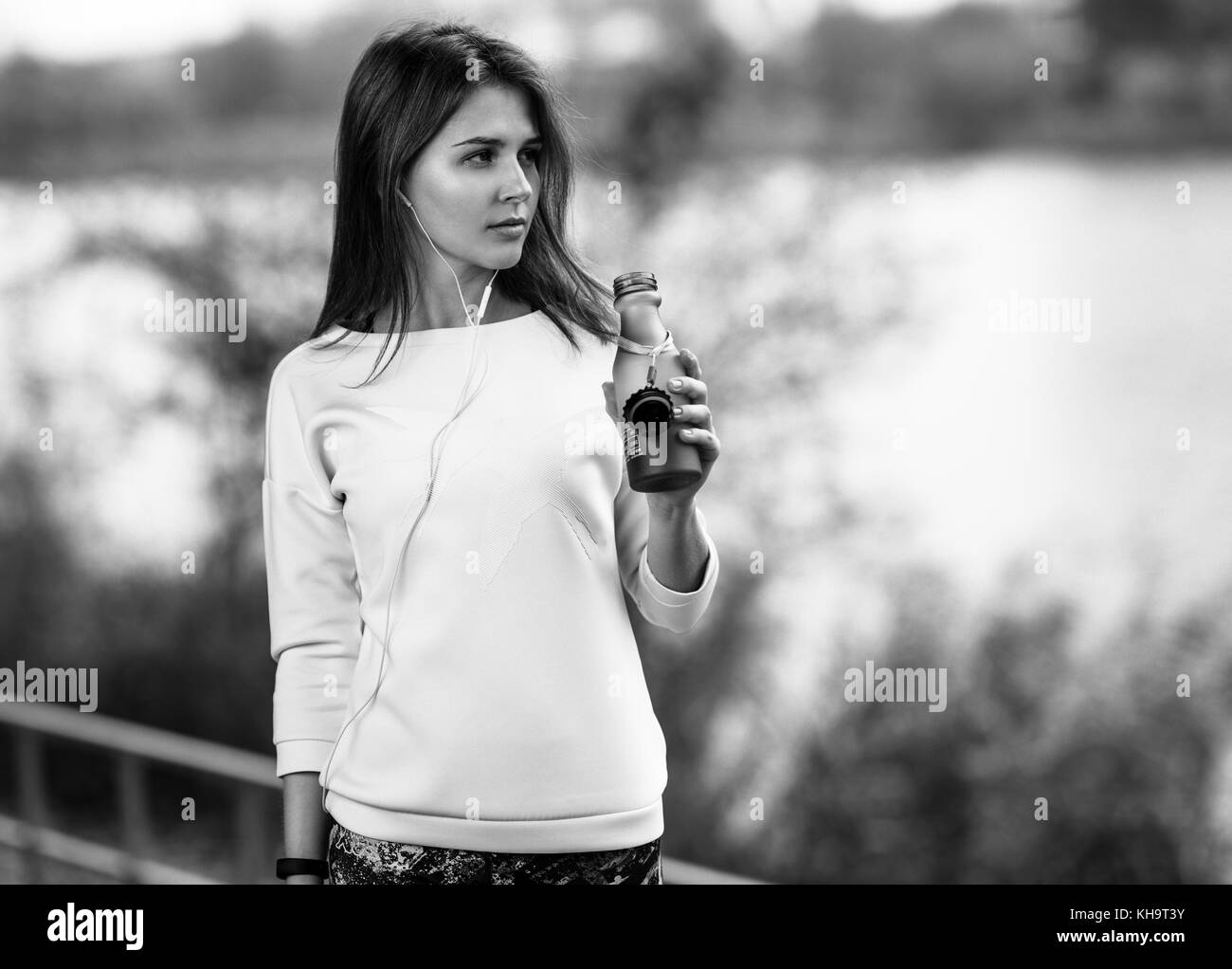 Young fitness girl with bottle of water standing outdoor in city park. Stock Photo