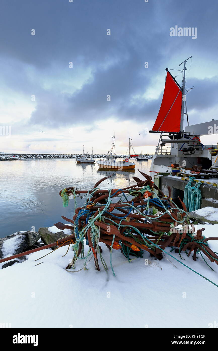 Bunch of oxidized five tined grapnel anchors and blue-green ropes on the snow covered pier-fishing boats moored in the port of Eggum ready to downdoad Stock Photo