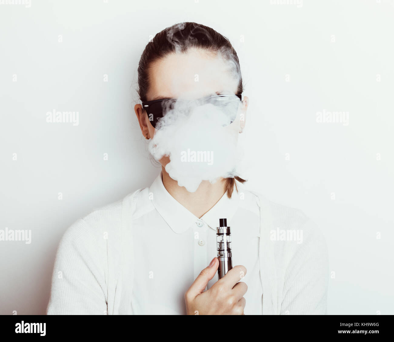 Woman in sunglasses smokes an ecigarette on a white background Stock