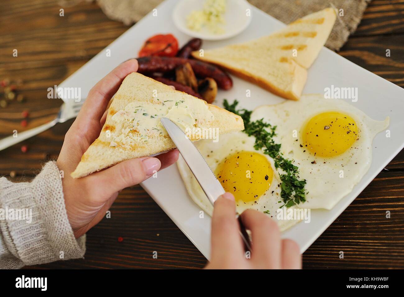 hand with a knife smears butter on bread close-up on a breakfast background Stock Photo