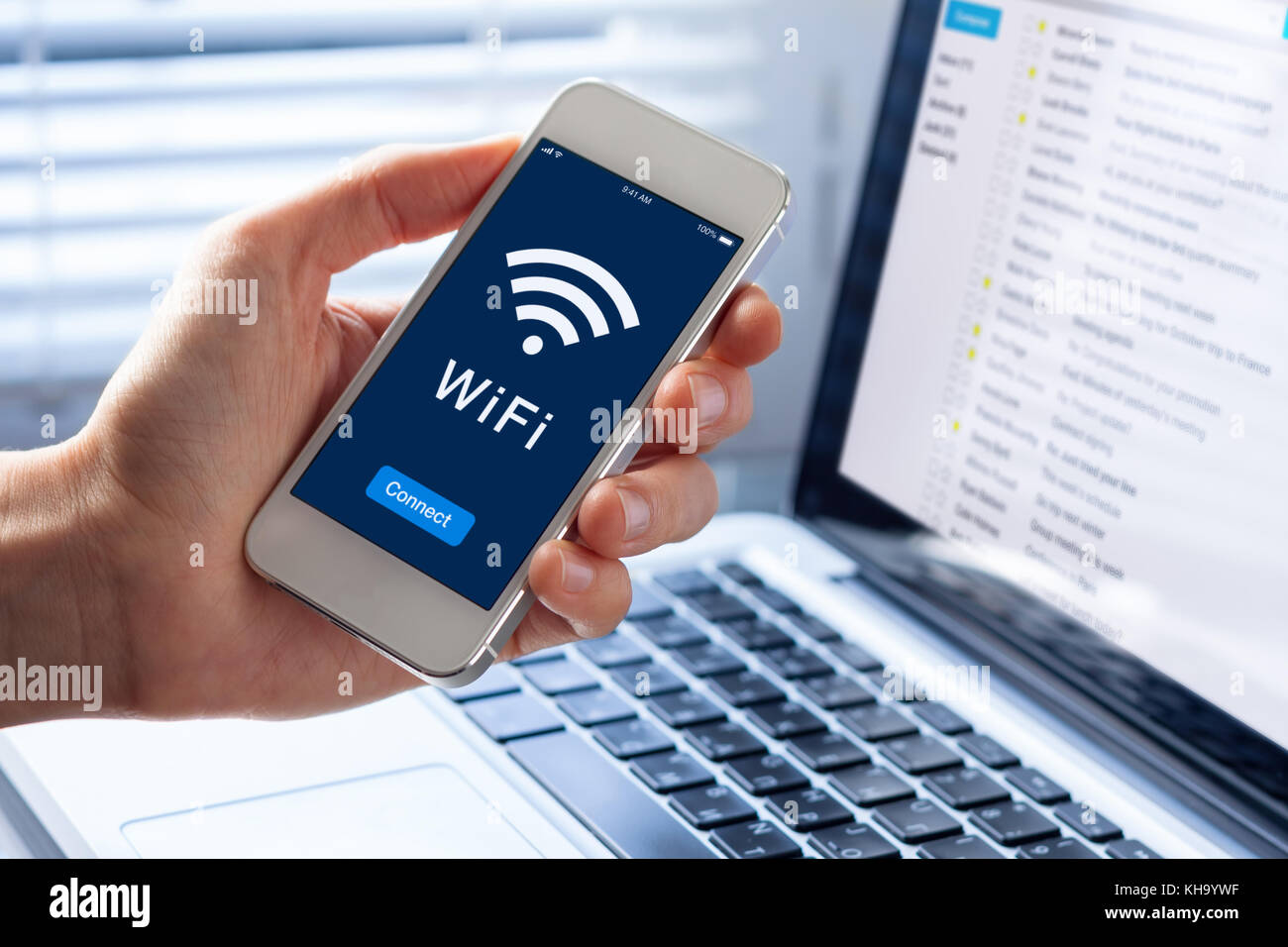 WiFi symbol on smartphone screen with button to connect to wireless internet, close-up of hand holding mobile phone, computer in background Stock Photo