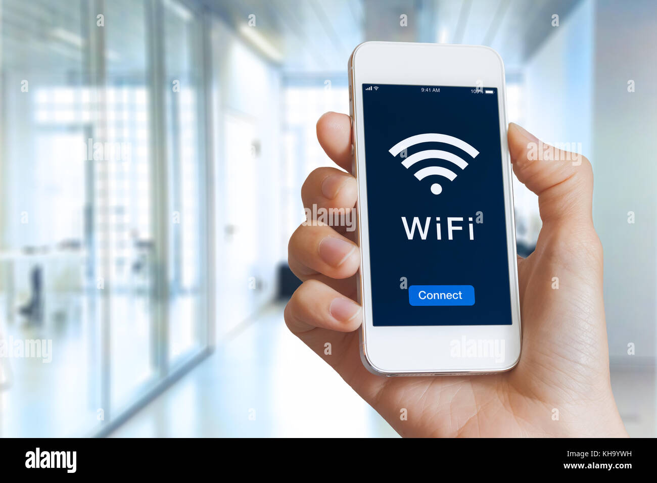 Close-up of hand holding smartphone with WiFi symbol and connect button on the screen to access public wireless internet, blurred building interior Stock Photo