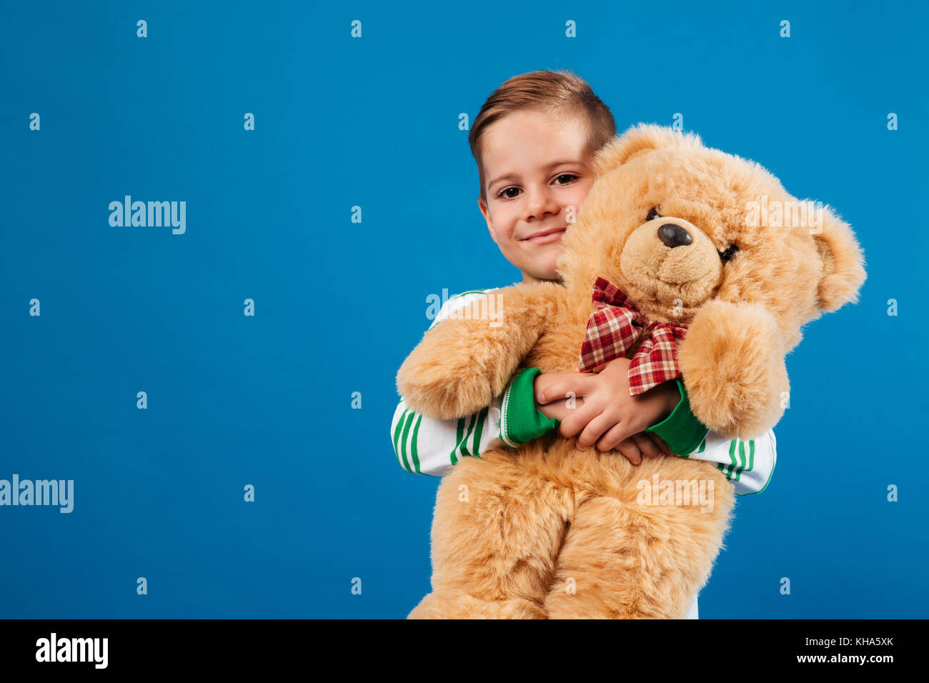Smiling young boy holding teddy bear and looking at the camera over ...