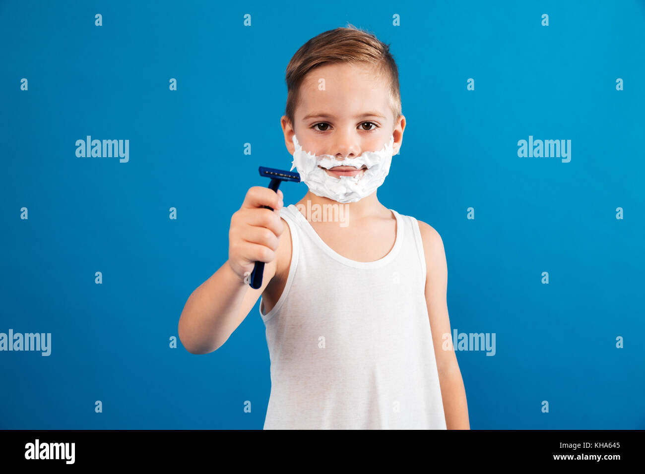 Smiling young boy in shaving foam showing razor like man and looking at ...