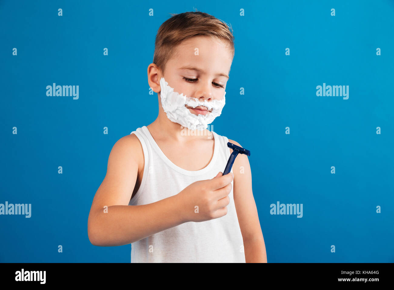 Picture of Smiling young boy in shaving foam like man looking at razor ...