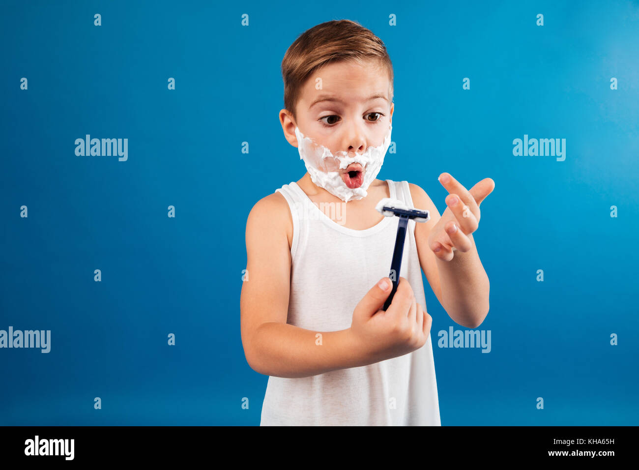 Shocked young boy in shaving foam like man holding razor and looking at ...