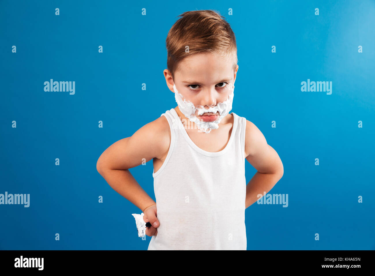 Serious young boy in shaving foam like man holding razor and looking at ...