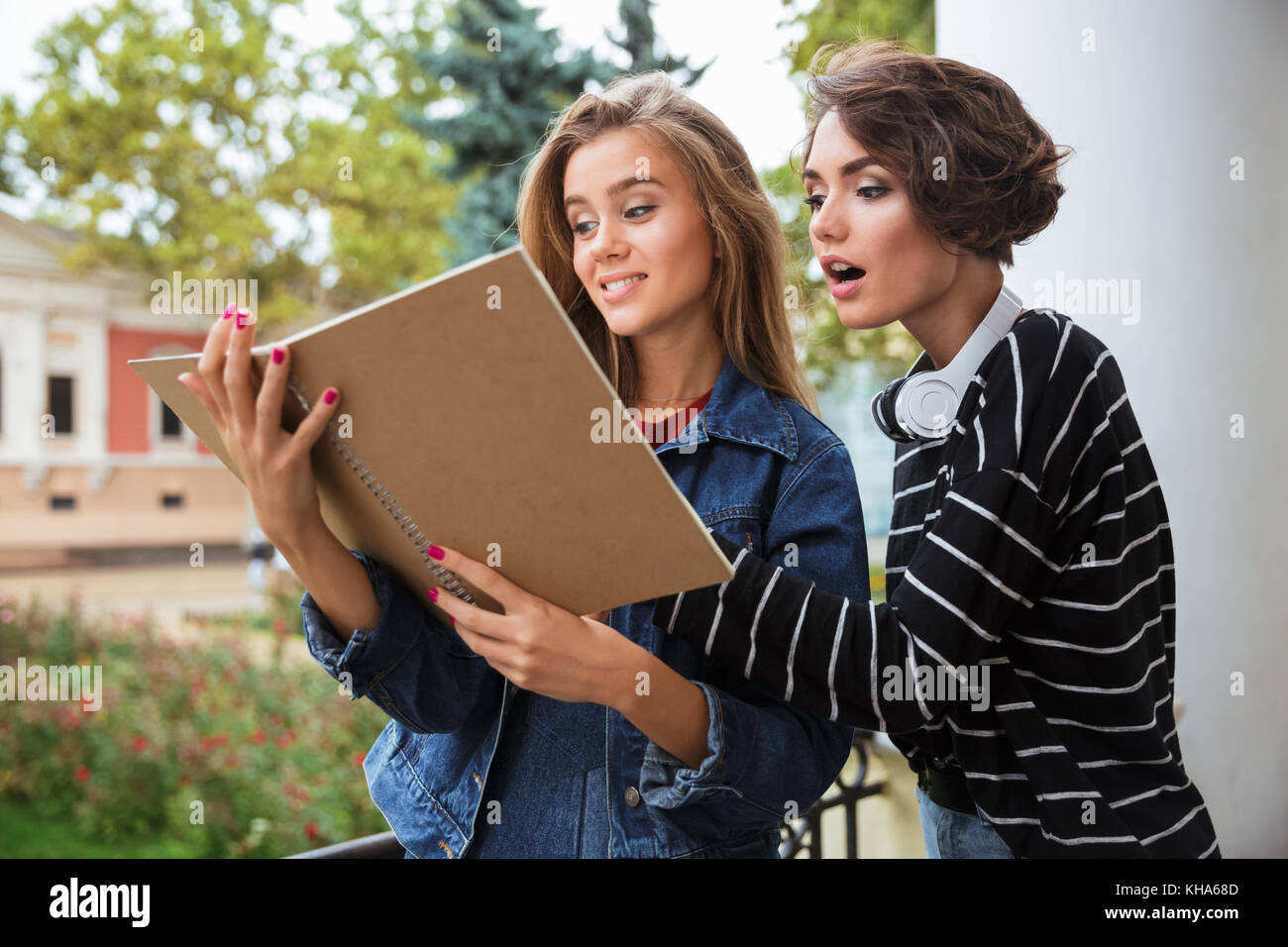 Two young pretty teenage girls studuing together with a book outdoors ...