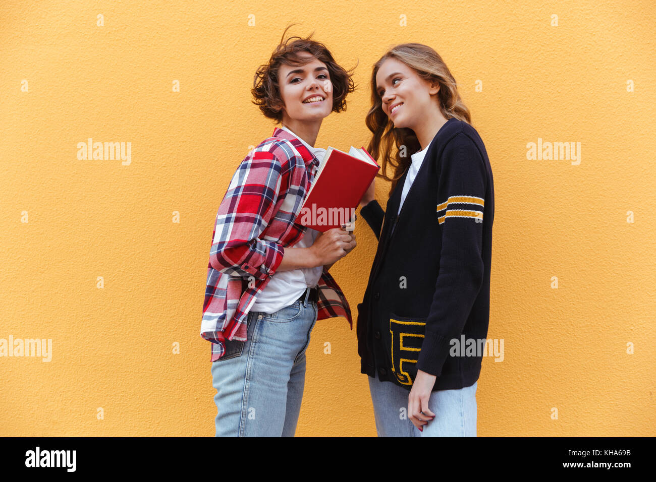 Two young teenage girls with books outdoors against orange wall Stock ...