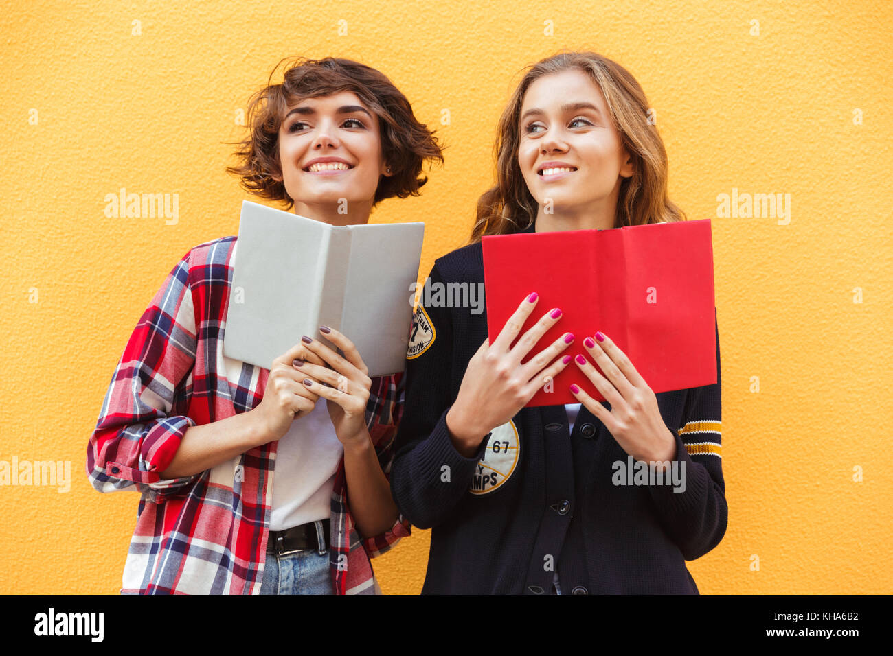 Portrait of two smiling pretty teenage girls with books standing and ...