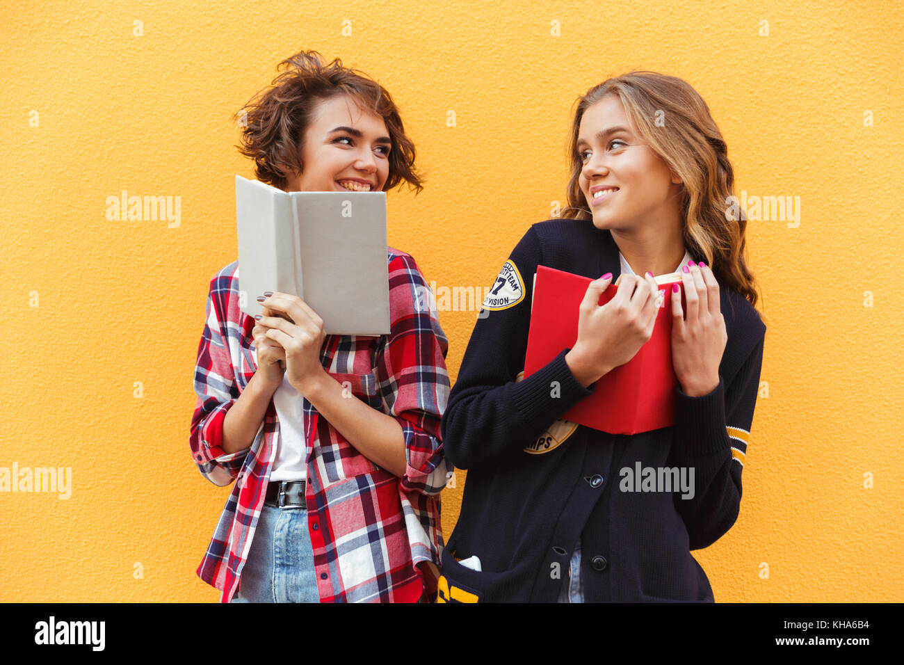 Portrait of two happy pretty teenage girls with books standing and ...