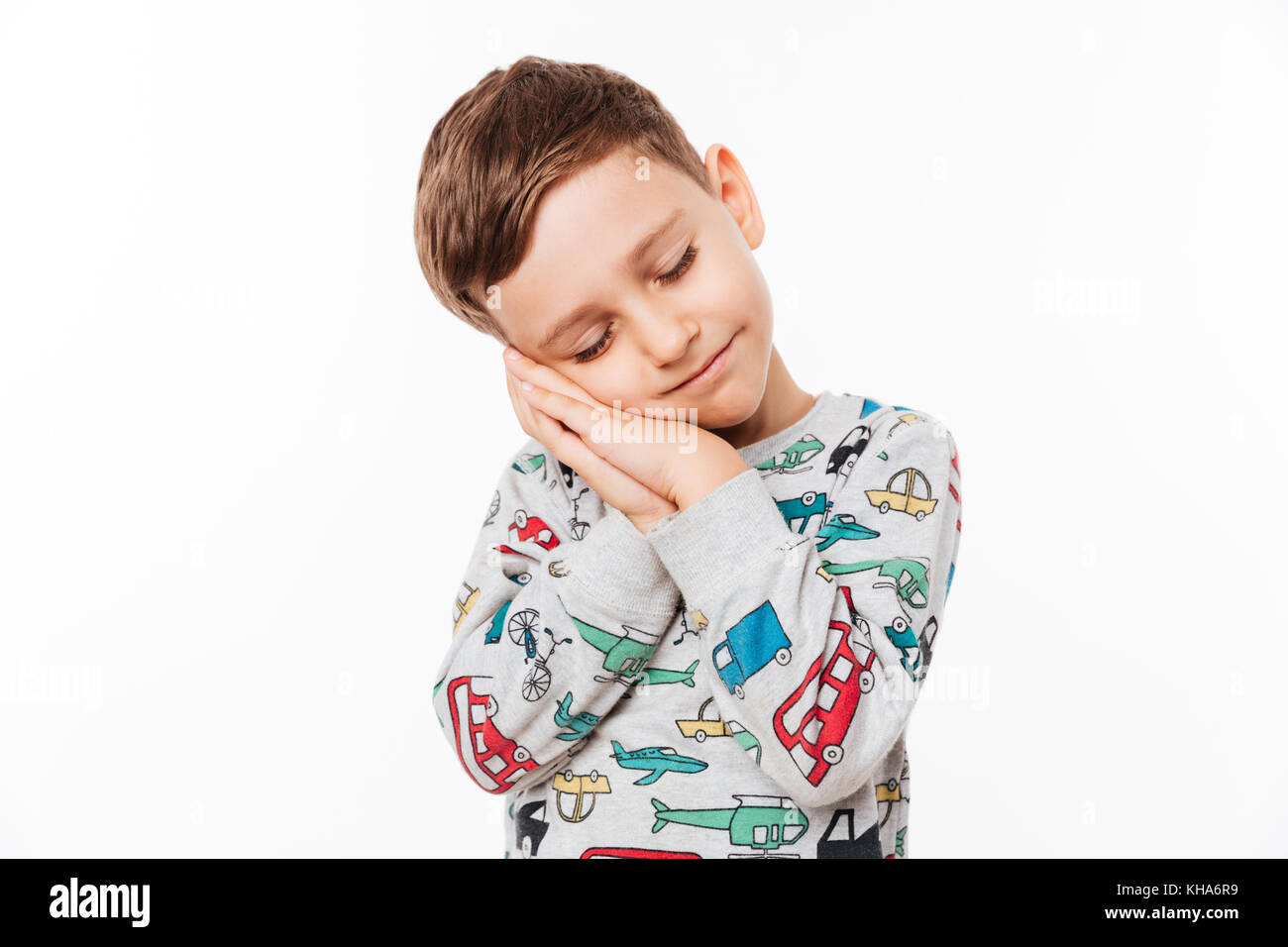 Portrait of a cute little kid standing with hands sealed pretending he is sleeping isolated over