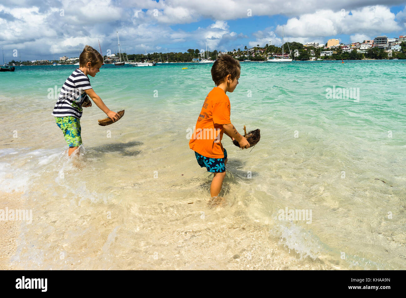 Two young boys, 5 and 7 years old, playing with small boat in coco ont he beach, Gosier island, Guadeloupe, France Stock Photo