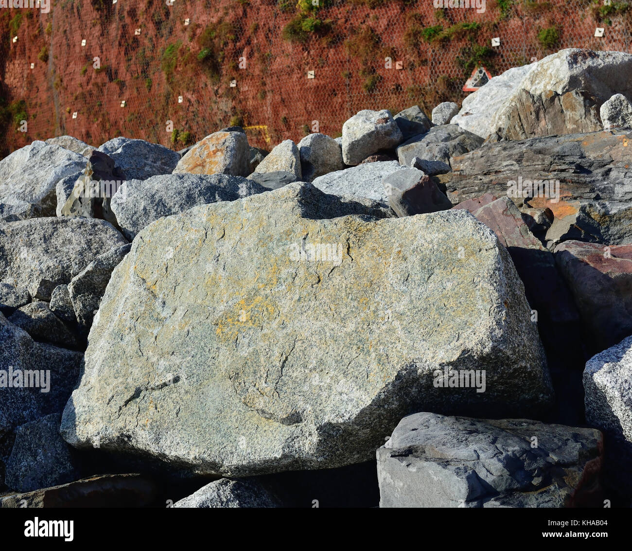 Rock armour large boulders piled against red sandstone cliffs to
