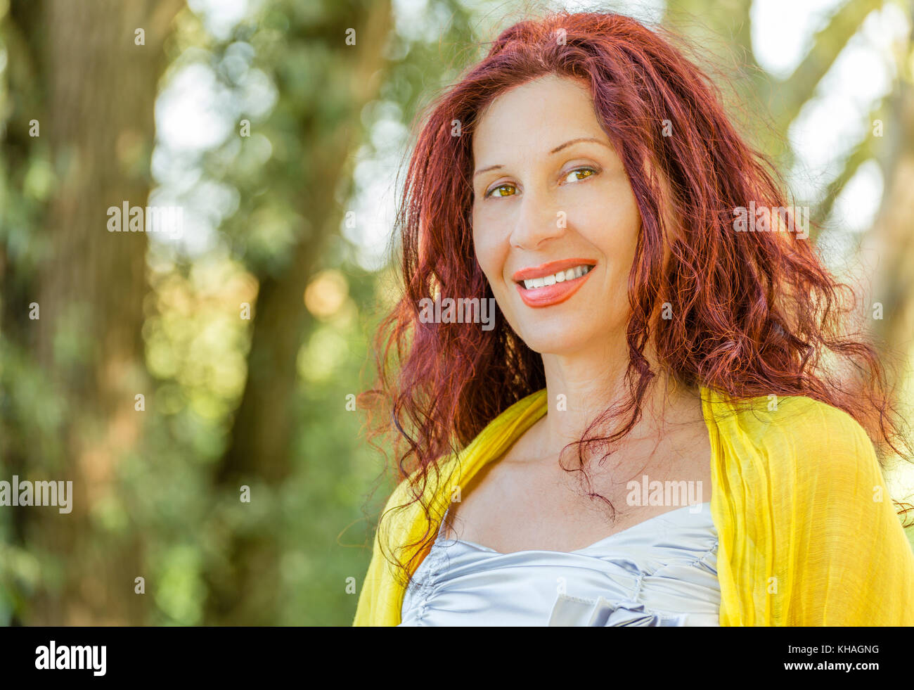 portrait of German mature woman with yellow  shawl and silver top smiling in a green garden Stock Photo