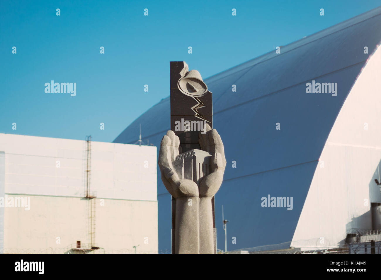 A memorial statue stands outside the Chernobyl power plant station dome (behind) in Ukraine Stock Photo