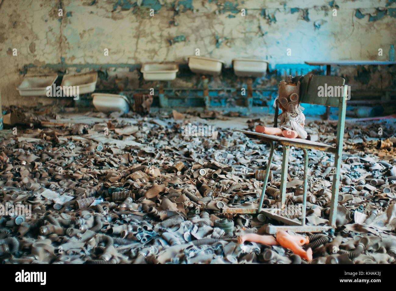 A child's doll is propped up on a chair in a sea of children's gas masks leftover from the Cold War in an abandoned school in Pripyat, Chernobyl Stock Photo