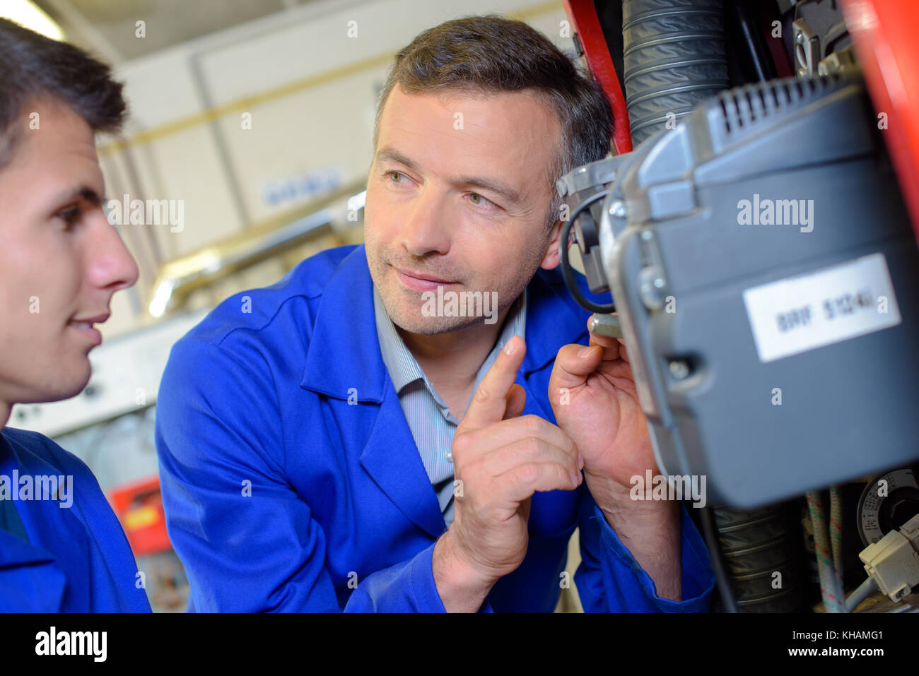 Teacher looking at motor, giving warning to apprentice Stock Photo - Alamy