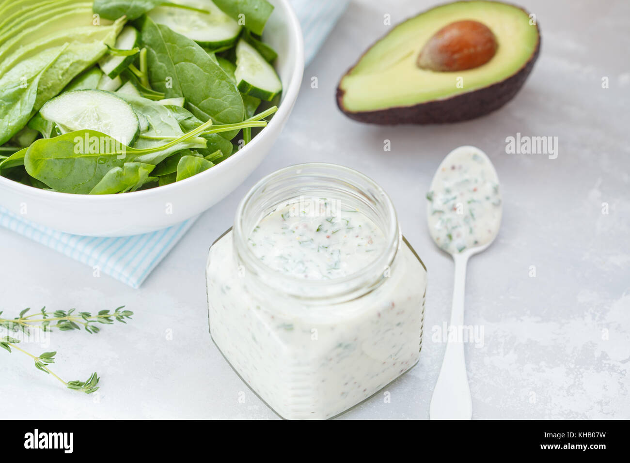 Yogurt mustard dressing to green spinach avocado salad, light background. Vegetarian healthy