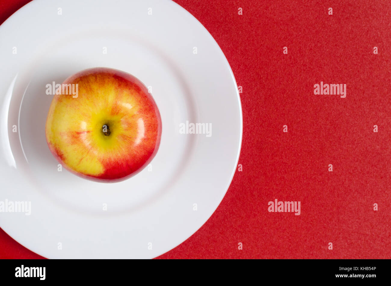 ripe red-yellow apple on a white plate against the red background Stock Photo