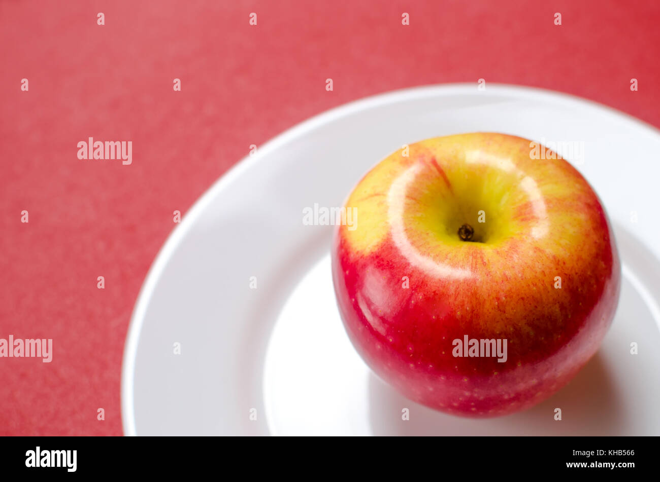 ripe red-yellow apple on a white plate against the red background Stock Photo