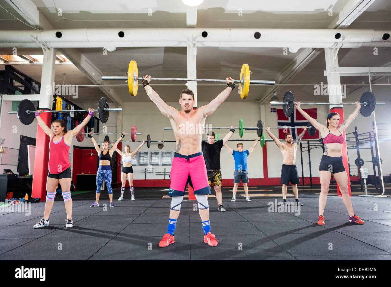 Determined trainer with male and female clients lifting barbells in fitness club Stock Photo