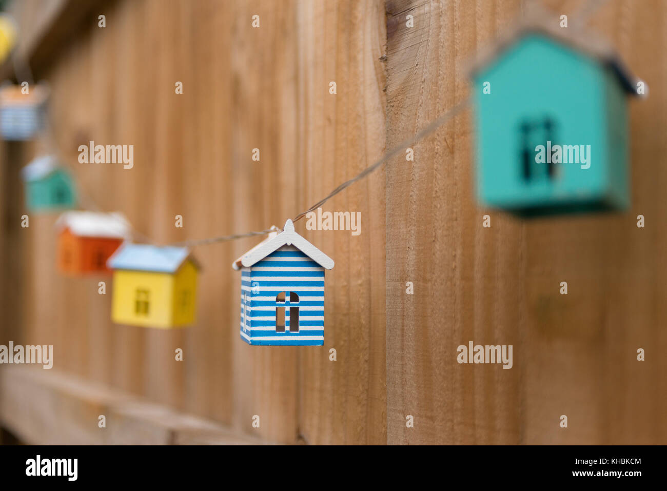 Colourful tiny model houses linked on a cord hanging on a fence. Stock Photo