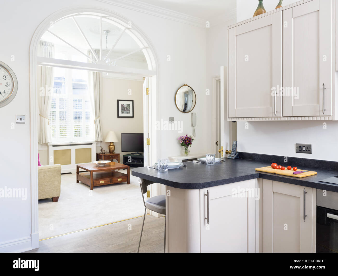 A fresh, light, traditional yet contemporary kitchen. furnished with fitted cabinets & a breakfast bar. With a view in to a living room. Stock Photo