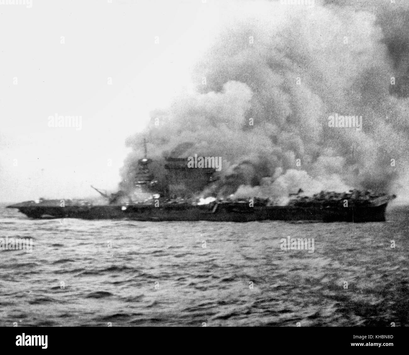 The U.S. Navy aircraft carrier USS Lexington (CV-2), burning and sinking after her crew abandoned ship during the Battle of Coral Sea, 8 May 1942. Note planes parked aft, where fires have not yet reached. Stock Photo