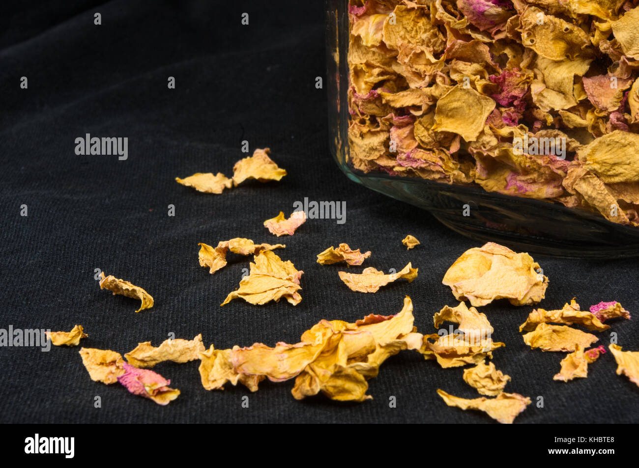 dried rose petals in a glass jar with lid on a black background Stock