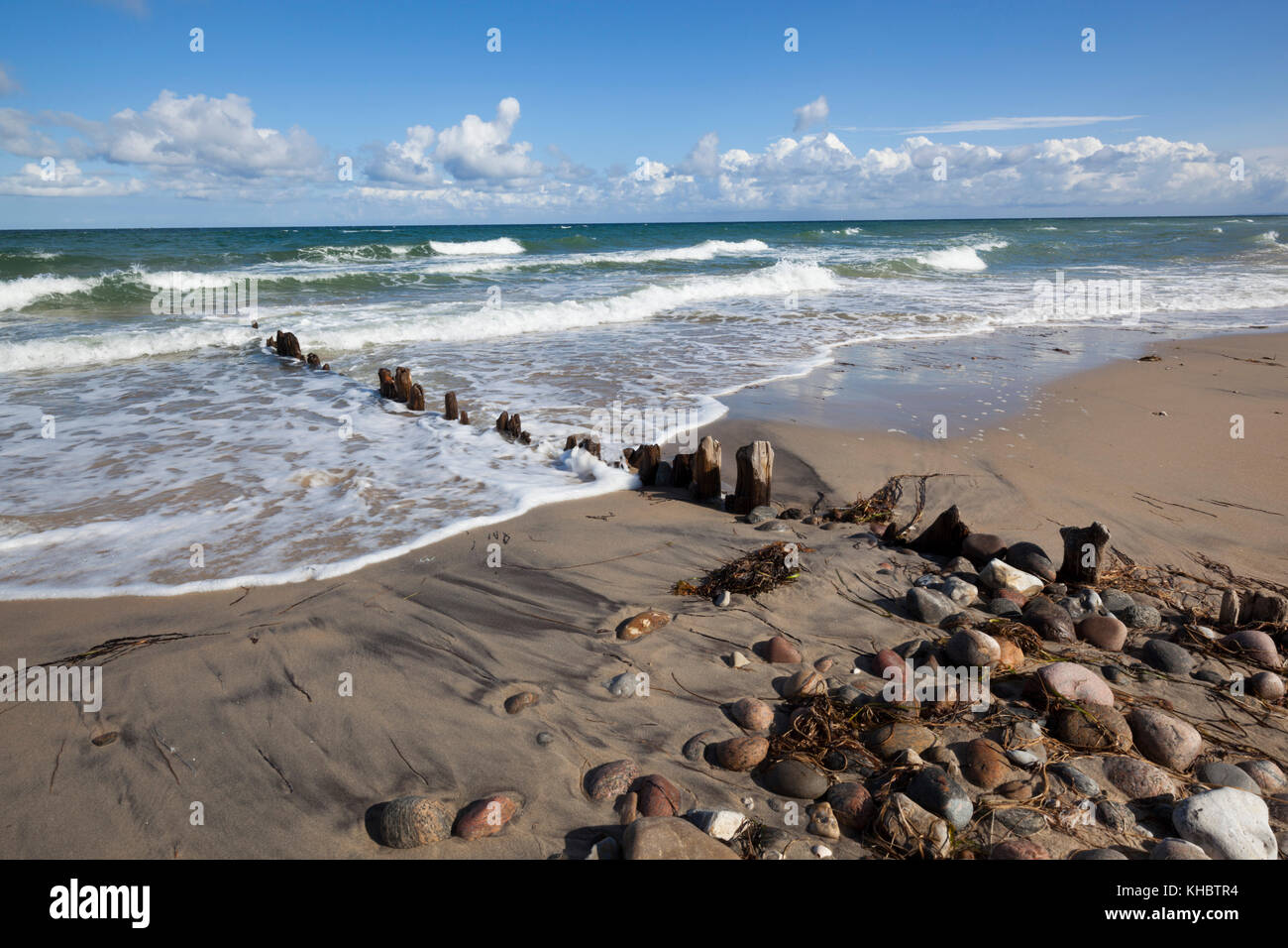 Old wooden posts and pebbles on sand beach with breaking waves and cumulus clouds, Rageleje, Kattegat Coast, Zealand, Denmark, Europe Stock Photo