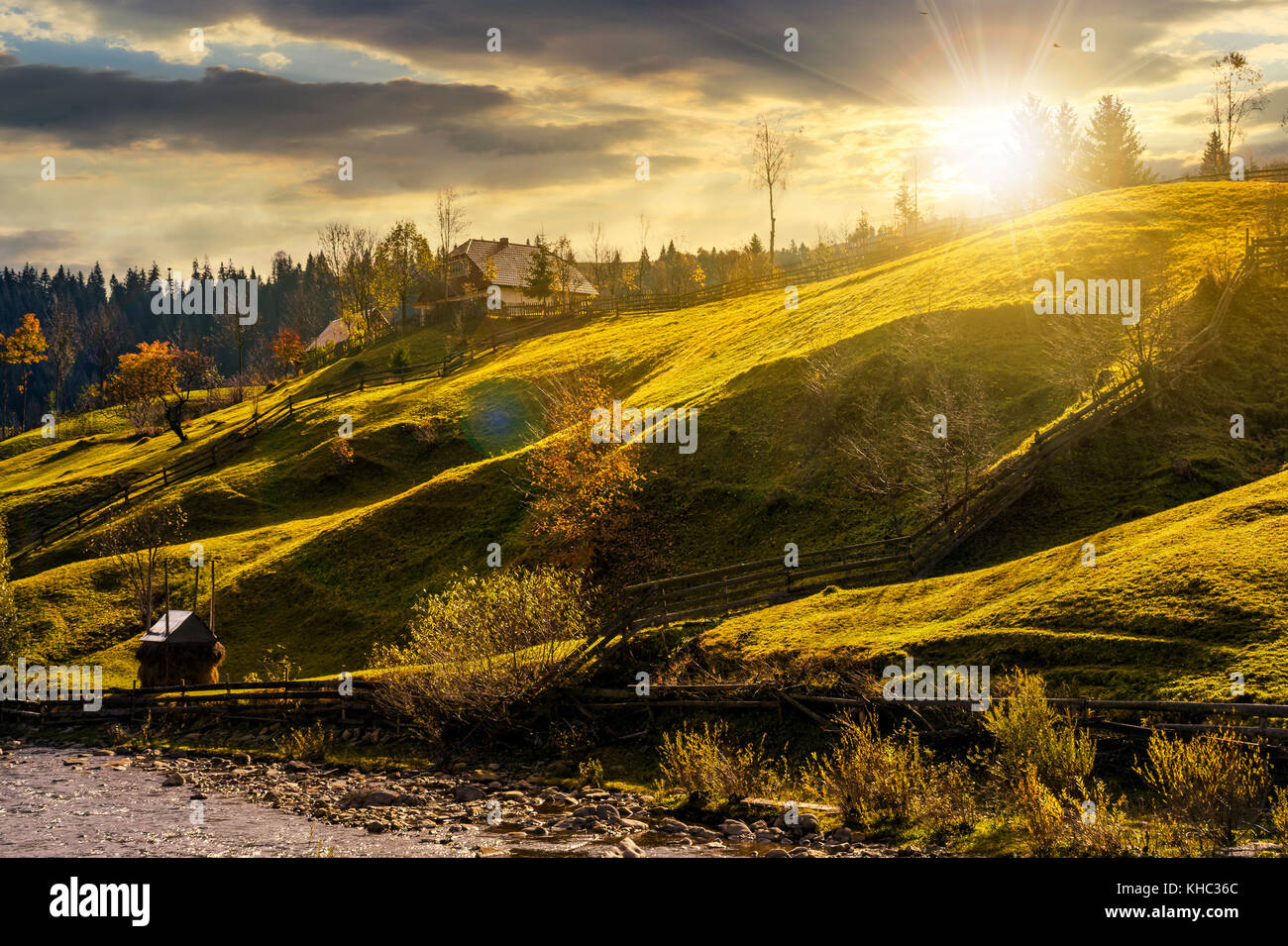 grassy rural hillside near the village at sunset. beautiful countryside scenery in autumn Stock Photo
