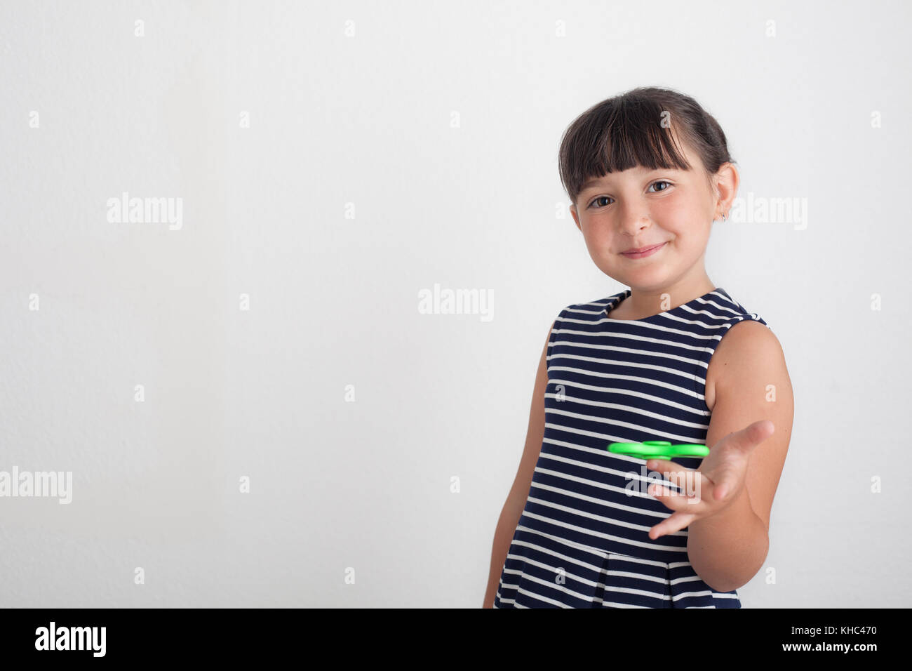 The 7 years old girl using a green fidget spinner against white backdrop. Stock Photo
