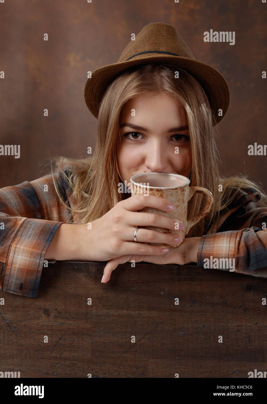 Young beautiful blonde in a brown plaid shirt with a mug of coffee .Natural old wooden background . Stock Photo
