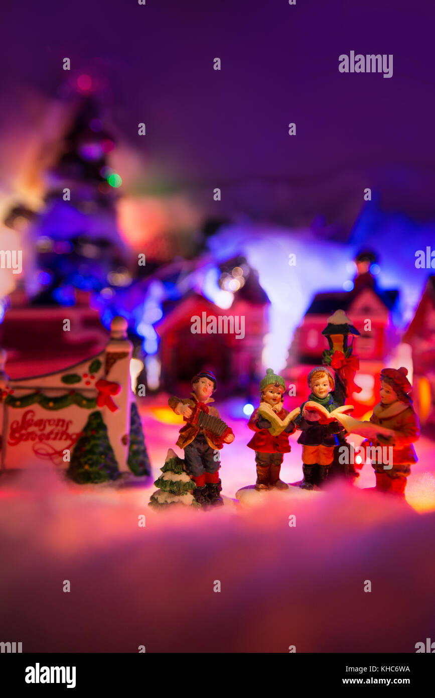 kid choir singing next to Seasons greeting sign with colorful christmas village in the background. Holiday greeting miniature scenery Stock Photo