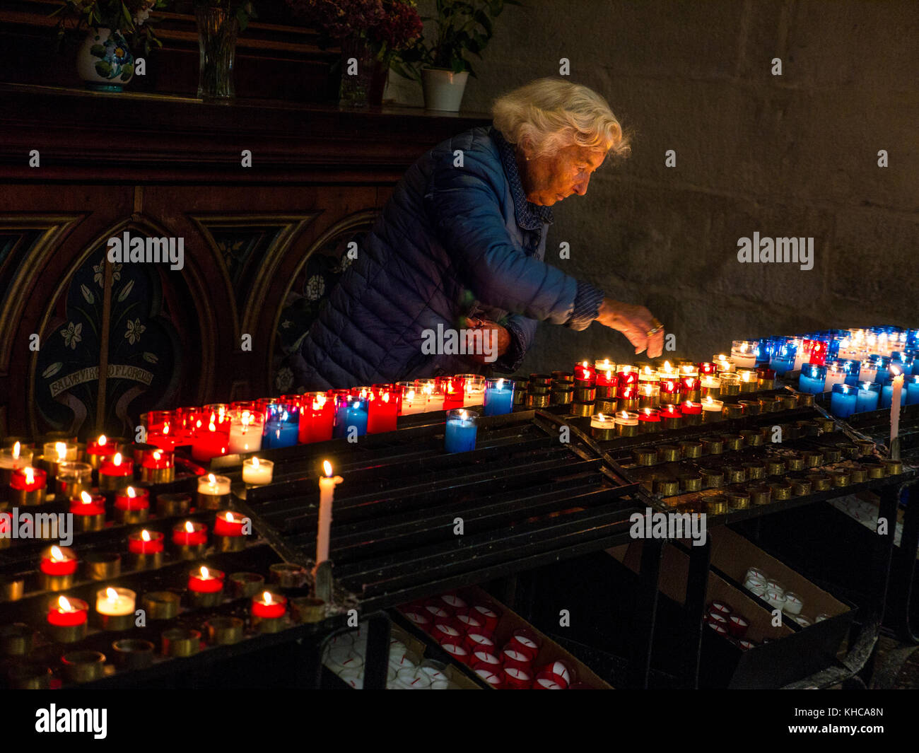 Covid Coronavirus death deaths concept church remembrance . Elderly lady places a lit candle inside a church as a token of respect and love to remember a dead lost loved one to the Covid 19 pandemic Stock Photo