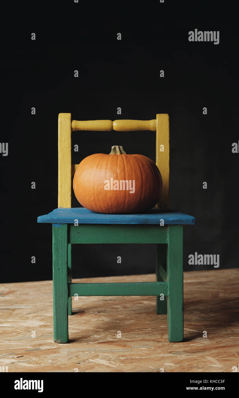 Round pumpkin Cucurbita or squash vegetable with a bright orange skin on a wooden chair, studio shot with dark background Stock Photo
