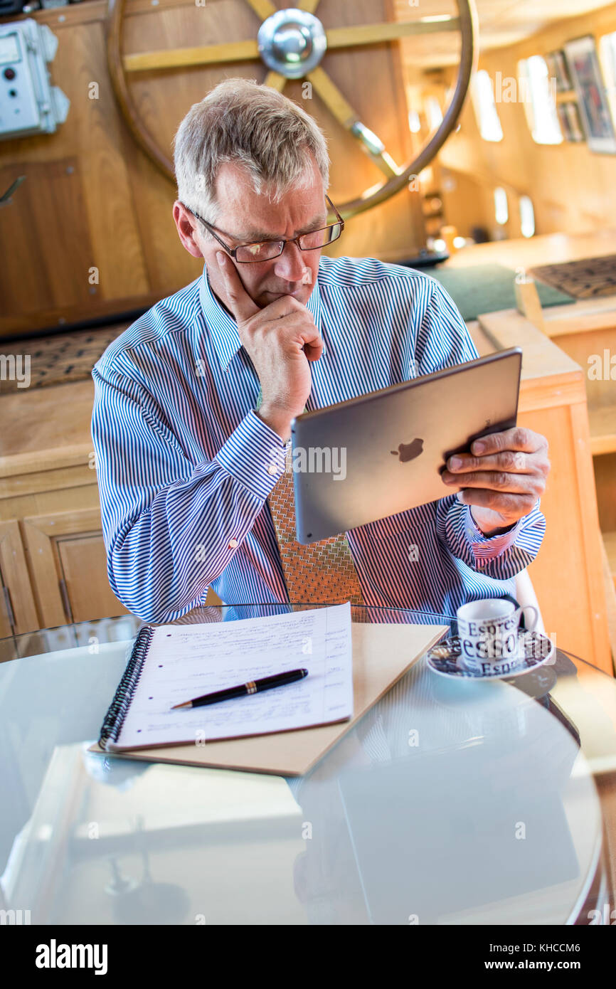 BOAT OFFICE LIFESTYLE WORK Mature businessman concentrating on his iPad air smart tablet computer screen in his houseboat home barge office London UK Stock Photo
